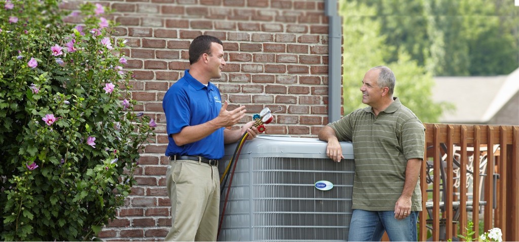 AC technician in blue shirt explaining AC Repairs to homeowner
